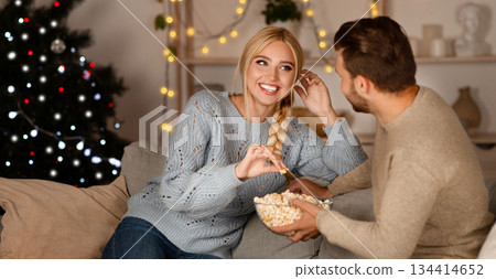 Joyful man and woman spending time at home during winter holidays, eating popcorn and laughing, copy space 134414652