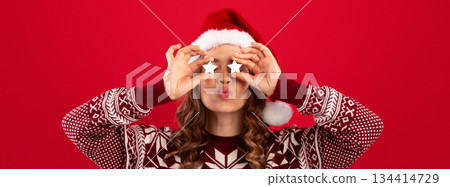 Lovely girl in Christmas clothes holding stars near her eyes and pursing lips for kiss, red background. Panorama Lovely girl in Christmas clothes holding stars near her eyes and pursing lips for kiss, red background. Panorama 134414729