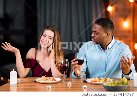 Annoyed African Man Looking At His Girlfriend Talking On Mobile Phone During Romantic Dinner In Restaurant, Complaining About Her Cellphone Addiction. Interracial Couple Having Communication Problems Annoyed African Man Looking At His Girlfriend Talking On Mobile Phone During Romantic Dinner In Restaurant, Complaining About Her Cellphone Addiction. Interracial Couple Having Communication Problems 134414787