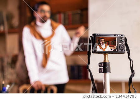 Teacher Blogger Guy Making Video Lesson For Educational Blog Standing Near Blackboard Indoor, Focus On Camera. E-Teaching And Online Learning, Knowledge And Modern Distance Education. Shallow Depth 134414793