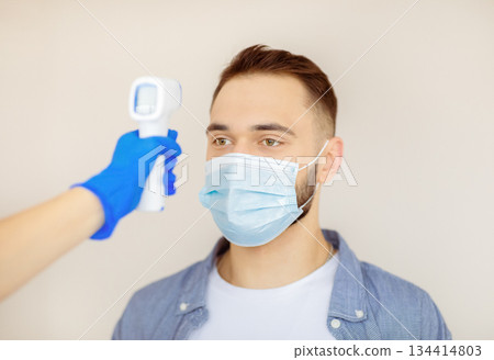 Doctor checking young man's temperature with digital thermometer before coronavirus immunization at clinic. Millennial guy in face mask visiting hospital for covid-19 vaccination Doctor checking young man's temperature with digital thermometer before coronavirus immunization at clinic. Millennial guy in face mask visiting hospital for covid-19 vaccination 134414803