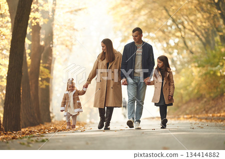 Autumn park. Happy family of mother, father and two daughters are in the forest, road Autumn park. Happy family of mother, father and two daughters are in the forest, road 134414882