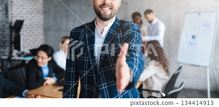 Successful Young Entrepreneur Stretching Hand For Handshake Greeting Smiling To Camera Standing In Modern Office. Employment And Business Career Offer Concept. Selective Focus Successful Young Entrepreneur Stretching Hand For Handshake Greeting Smiling To Camera Standing In Modern Office. Employment And Business Career Offer Concept. Selective Focus 134414913