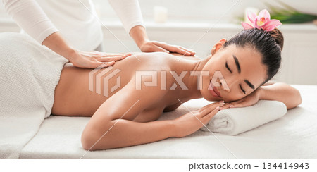 Relaxed asian woman enjoying body massage at spa, getting treatment with professional masseur in beauty parlor, lying on table with closed eyes, having wellness day, side view with free space Relaxed asian woman enjoying body massage at spa, getting treatment with professional masseur in beauty parlor, lying on table with closed eyes, having wellness day, side view with free space 134414943