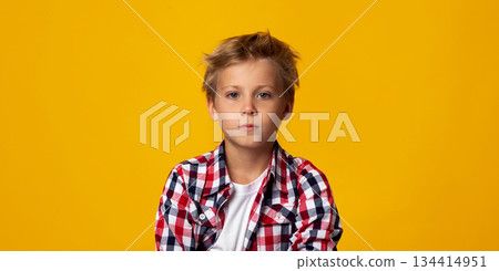 Serious seriously calm cute caucasian teenage boy looking at camera, isolated on yellow background, copy space, panorama, studio shot. Sad tired child, feeling unwell and despair facial expression 134414951