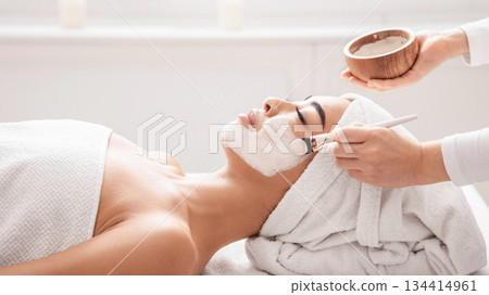 Skin Lifting Treatment. Young asian woman getting facial nourishing mask by professional beautician at spa salon, calm lady enjoying wellness day and beauty procedures, side view with copy space 134414961