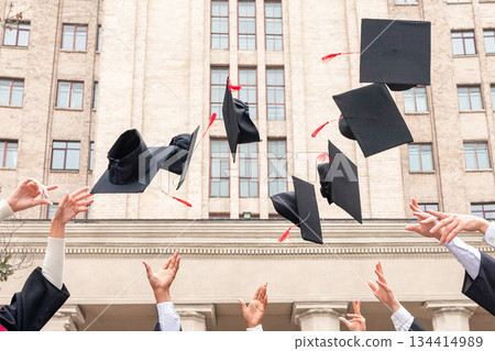 Multiracial group of students standing in a row and throwing graduation caps up in the air, posing next to university building after graduation ceremony, celebrating freedom, panorama with copy space Multiracial group of students standing in a row and throwing graduation caps up in the air, posing next to university building after graduation ceremony, celebrating freedom, panorama with copy space 134414989