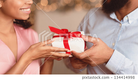 Closeup of happy lovers exchanging gifts on holiday, anniversary, St Valentine's day or birthday. Happy attractive young african american female giving or receiving present surprise from her man Closeup of happy lovers exchanging gifts on holiday, anniversary, St Valentine's day or birthday. Happy attractive young african american female giving or receiving present surprise from her man 134414998
