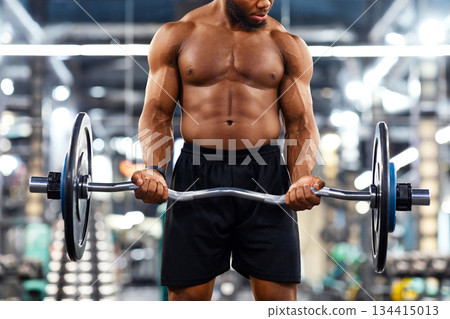 Athletic black man making weightlifting or powerlifting, working on arms and chest musculs with heavy barbell, gym interior. Muscular shirtless african american bodybuilder powerlifting, copy space 134415013