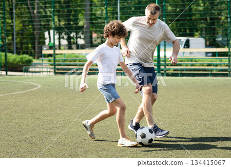 Active Lifestyle. Full length portrait of sportive father playing soccer with his son on green grass at stadium 134415067