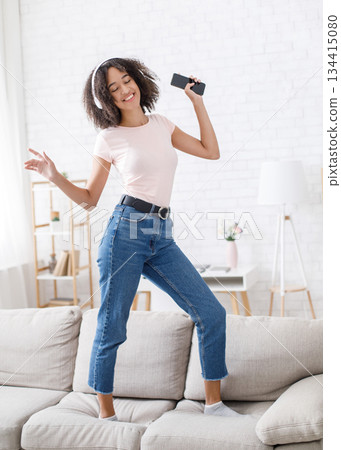 Musical break. African american girl enjoying music and dancing on couch at home during work or study, free space, vertical photo Musical break. African american girl enjoying music and dancing on couch at home during work or study, free space, vertical photo 134415080