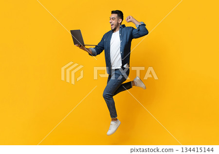 Emotional arab young man jumping up, using new modern laptop, raising fist up and smiling over yellow studio background, trading online, copy space for text or advertisement, panorama Emotional arab young man jumping up, using new modern laptop, raising fist up and smiling over yellow studio background, trading online, copy space for text or advertisement, panorama 134415144