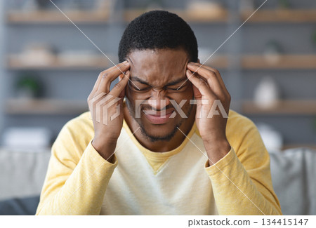 Closeup of young african american man suffering from headache at home, touching his temples, copy space, blurred background. Migraine, headache, stress, tension problem, hangover concept 134415147