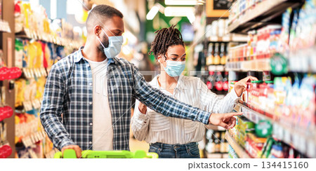 African Husband And Wife In Protective Face Masks Shopping Groceries In Supermarket Buying Food Essentials Walking With Shop Trolley Cart In Grocery Store Indoor. Family Preparing For Quarantine African Husband And Wife In Protective Face Masks Shopping Groceries In Supermarket Buying Food Essentials Walking With Shop Trolley Cart In Grocery Store Indoor. Family Preparing For Quarantine 134415160