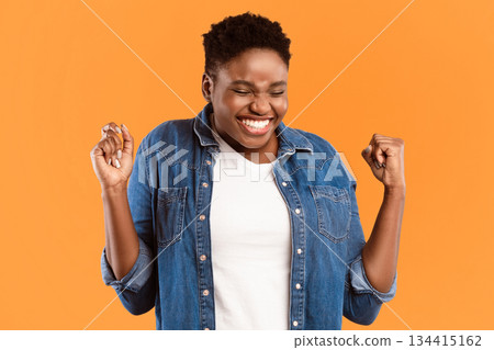 Yes. Joyful Plus Size Black Lady Shaking Fists In Joy Celebrating Success Standing Over Yellow Studio Background. Great News And Victory Celebration, Positive Emotions, Excitement Concept 134415162