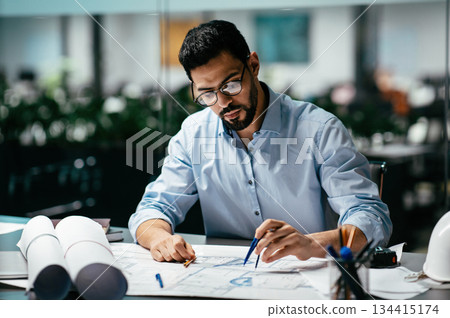 Concentrated busy handsome millennial islamic male engineer with beard in glasses, think about project in office interior, professional architect work in factory. Solving construction planning problem 134415174