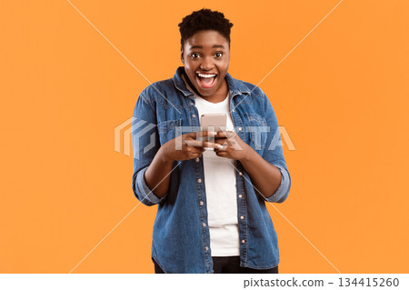 Great Application. Joyful Black Female Using New Smartphone And Mobile App Posing Smiling To Camera Standing Over Yellow Studio Background. Woman Playing Games On Phone Concept Great Application. Joyful Black Female Using New Smartphone And Mobile App Posing Smiling To Camera Standing Over Yellow Studio Background. Woman Playing Games On Phone Concept 134415260