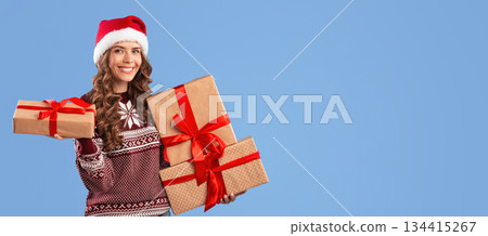 Happy young woman in Santa hat and Xmas sweater holding Christmas gifts on blue studio background, panorama. Portrait of pretty lady with wrapped presents for winter holidays looking at camera Happy young woman in Santa hat and Xmas sweater holding Christmas gifts on blue studio background, panorama. Portrait of pretty lady with wrapped presents for winter holidays looking at camera 134415267