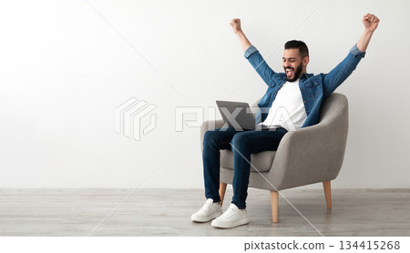 Overjoyed millennial Arab man sitting in armchair with laptop, celebrating online win or work success against white studio wall, copy space. Young Eastern guy enjoying big sale in web store, banner Overjoyed millennial Arab man sitting in armchair with laptop, celebrating online win or work success against white studio wall, copy space. Young Eastern guy enjoying big sale in web store, banner 134415268