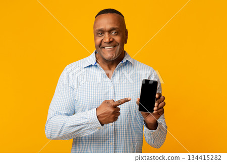 Awesome application or website. Middle aged black man showing blank cellphone screen, orange background with empty space Awesome application or website. Middle aged black man showing blank cellphone screen, orange background with empty space 134415282