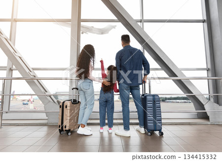 Cute Little Girl Standing With Parents In Airport Terminal, Looking At Plane Out Of Window, Rear View. Middle Eastern Family Of Three Waiting For Flight Boarding, Ready For Vacation Travel Together Cute Little Girl Standing With Parents In Airport Terminal, Looking At Plane Out Of Window, Rear View. Middle Eastern Family Of Three Waiting For Flight Boarding, Ready For Vacation Travel Together 134415332