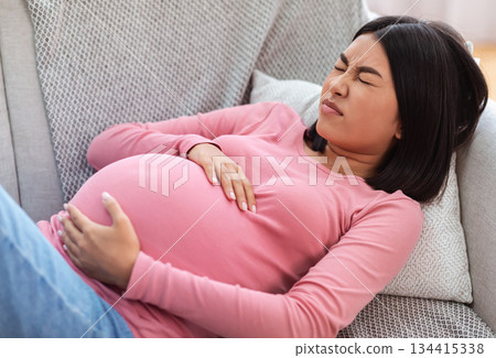 Pregnant Chinese Lady Suffering From Pain Touching Belly Having Painful Contractions Spasms Lying On Sofa At Home. Pregnancy Problems And Issues, Spontaneous Preterm Labour Concept 134415338