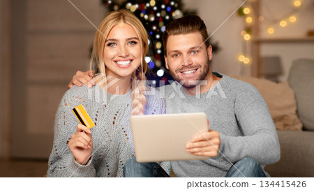 Happy family husband and wife shopping online, using digital tablet and credit card, xmas atmosphere at home. Happy young family purchasing online on pad, using Christmas discounts, copy space Happy family husband and wife shopping online, using digital tablet and credit card, xmas atmosphere at home. Happy young family purchasing online on pad, using Christmas discounts, copy space 134415426