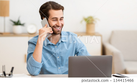 Gladful Man Talking On Phone Working On Laptop Online Sitting At Desk In Modern Office. Freelancer Guy Calling Speaking By Cellphone Indoors. Modern Mobile Communication Concept Gladful Man Talking On Phone Working On Laptop Online Sitting At Desk In Modern Office. Freelancer Guy Calling Speaking By Cellphone Indoors. Modern Mobile Communication Concept 134415466