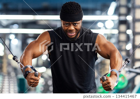 Motivated young black sportsman having workout on crossover machine. Handsome african american man bodybuilder training triceps on modern block exerciser in gym, copy space 134415467