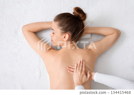 Top view of young lady having healing full body massage from unrecognizable female therapist at luxury spa. Beautiful naked woman getting relaxing back massage on white, view above 134415468