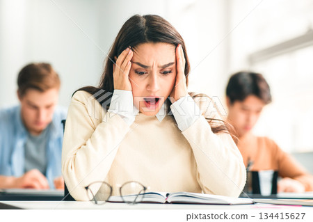 Portrait of shocked female student sitting at desk in classroom, grabbing her head looking at exam questions or results. Worried youth unprepared for test, thinking about deadline or low score Portrait of shocked female student sitting at desk in classroom, grabbing her head looking at exam questions or results. Worried youth unprepared for test, thinking about deadline or low score 134415627