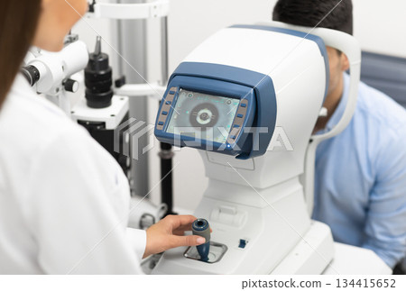 Eye Inspection Concept. Female ophthalmologist checking eye vision of young male customer in modern clinic, back view Eye Inspection Concept. Female ophthalmologist checking eye vision of young male customer in modern clinic, back view 134415652