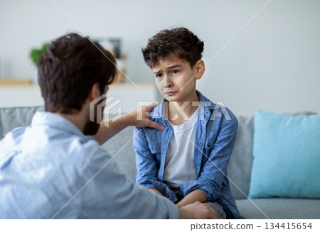 Father and sad son having heart to heart talk at home, daddy trying to solve problems, searching solution together. Parent showing care and love, calming down boy and holding hand on shoulder Father and sad son having heart to heart talk at home, daddy trying to solve problems, searching solution together. Parent showing care and love, calming down boy and holding hand on shoulder 134415654