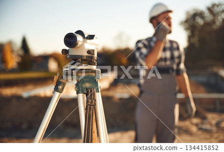 Geodetic optical level. Worker is on the construction site at daytime 134415852