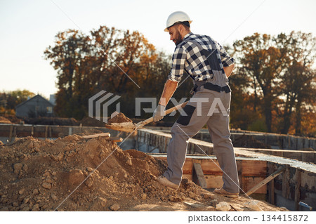 Digging, using shovel. Worker is on the construction site at daytime 134415872