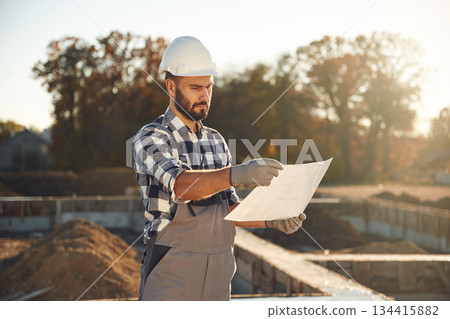 Holding plan in hands. Worker is on the construction site at daytime 134415882