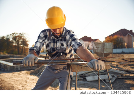 Working with metal rod. Man is on the construction site at daytime Working with metal rod. Man is on the construction site at daytime 134415908