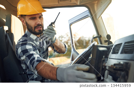 Holding radio, walkie talkie. Construction worker is sitting in the truck cabin Holding radio, walkie talkie. Construction worker is sitting in the truck cabin 134415959