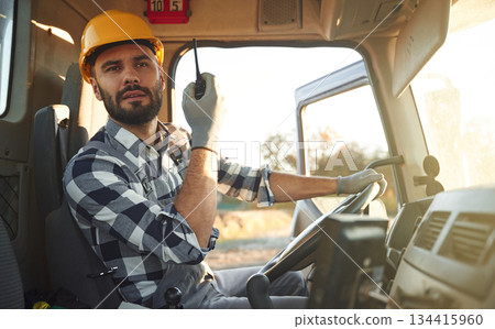 Holding radio, walkie talkie. Construction worker is sitting in the truck cabin 134415960