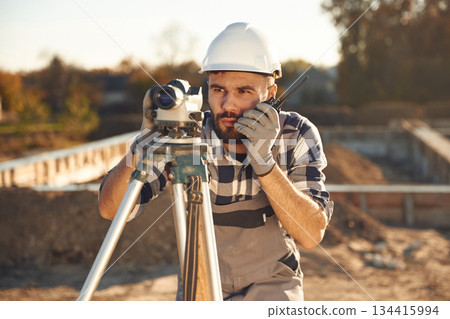 Front view, using geodetic optical level. Worker is on the construction site at daytime 134415994