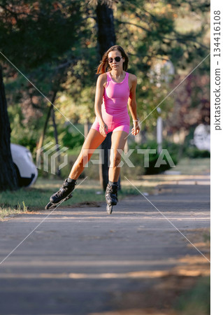 Woman in pink sportwear roller skating in the park, active lifestyle concept. 134416108