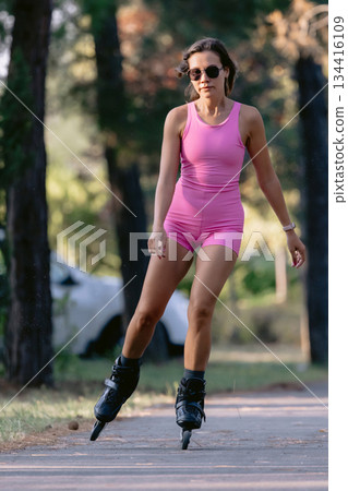 Woman in pink sportwear roller skating in the park, active lifestyle concept. 134416109