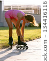 Woman in pink sportswear corrects rollerblades outdoor on a sunny summer day 134416116