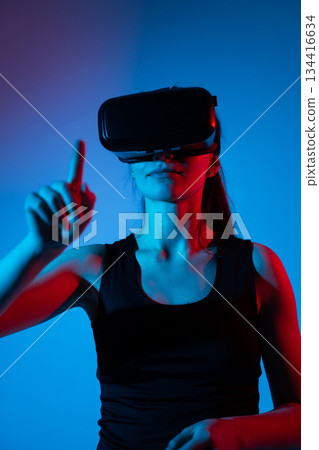 Woman using VR headset with neon blue and red light, interacting in virtual reality environment Woman using VR headset with neon blue and red light, interacting in virtual reality environment 134416634