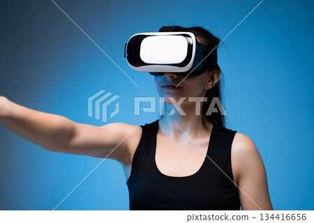 Female user interacting with VR interface while wearing headset in futuristic digital reality scene 134416656