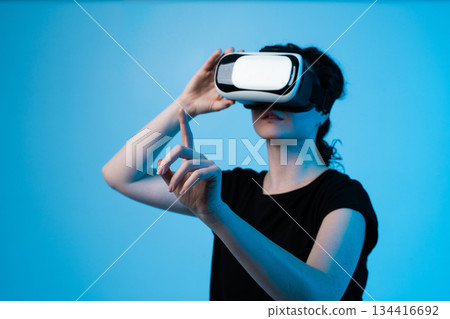 Woman using VR headset in profile while adjusting goggles and interacting with virtual environment Woman using VR headset in profile while adjusting goggles and interacting with virtual environment 134416692