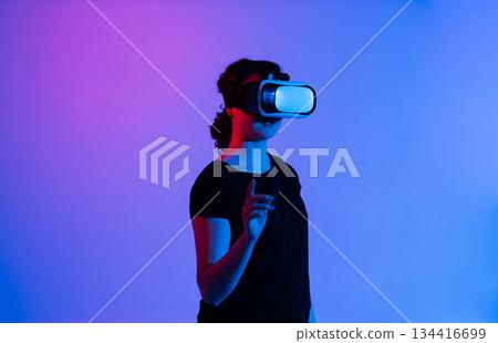 VR headset woman interacting with virtual elements while illuminated by vivid neon blue and pink studio lighting VR headset woman interacting with virtual elements while illuminated by vivid neon blue and pink studio lighting 134416699