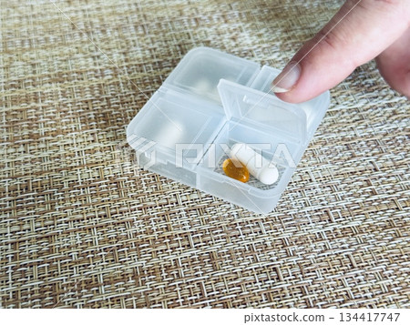 The weekly transparent pill box is designed for convenient and efficient daily storage of dietary supplements and pills. The woman's finger points to the capsule compartment. 134417747