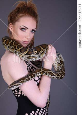 Beautiful redhead girl posing with her pet snake in the studio Beautiful redhead girl posing with her pet snake in the studio 134418051