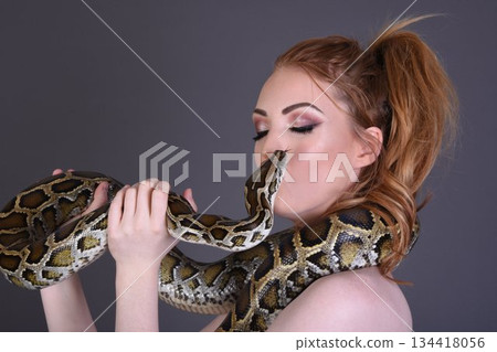 Beautiful redhead girl posing with her pet snake in the studio Beautiful redhead girl posing with her pet snake in the studio 134418056